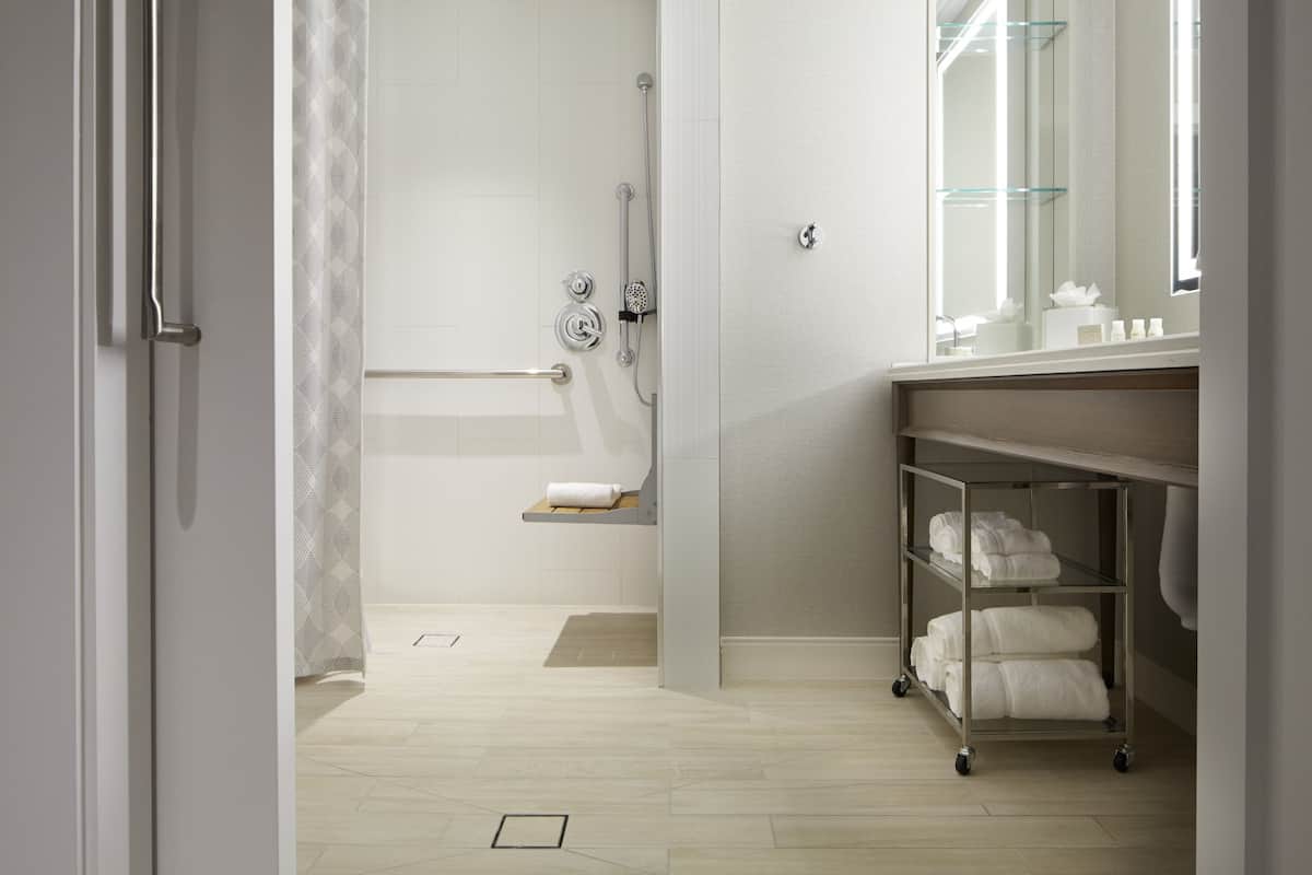 Un baño moderno con ducha, toallero y repisa con toallas.