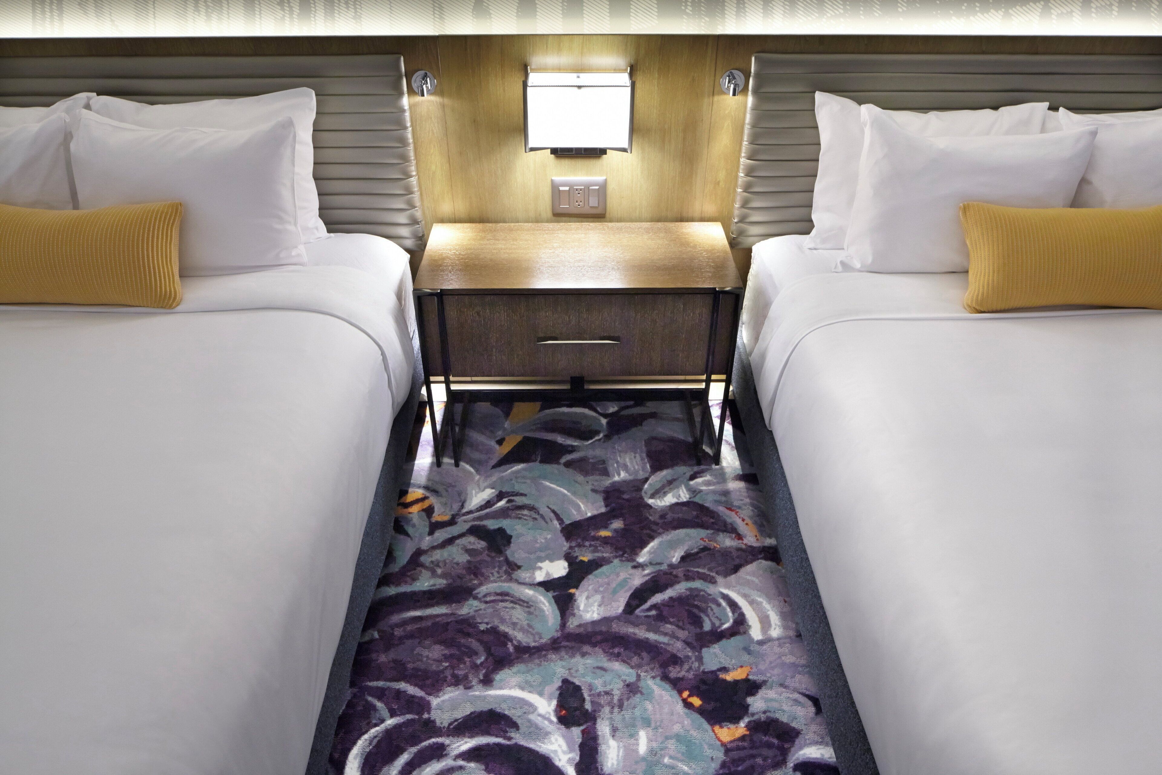 A hotel room with two beds, a nightstand, and a carpet with a wave pattern.