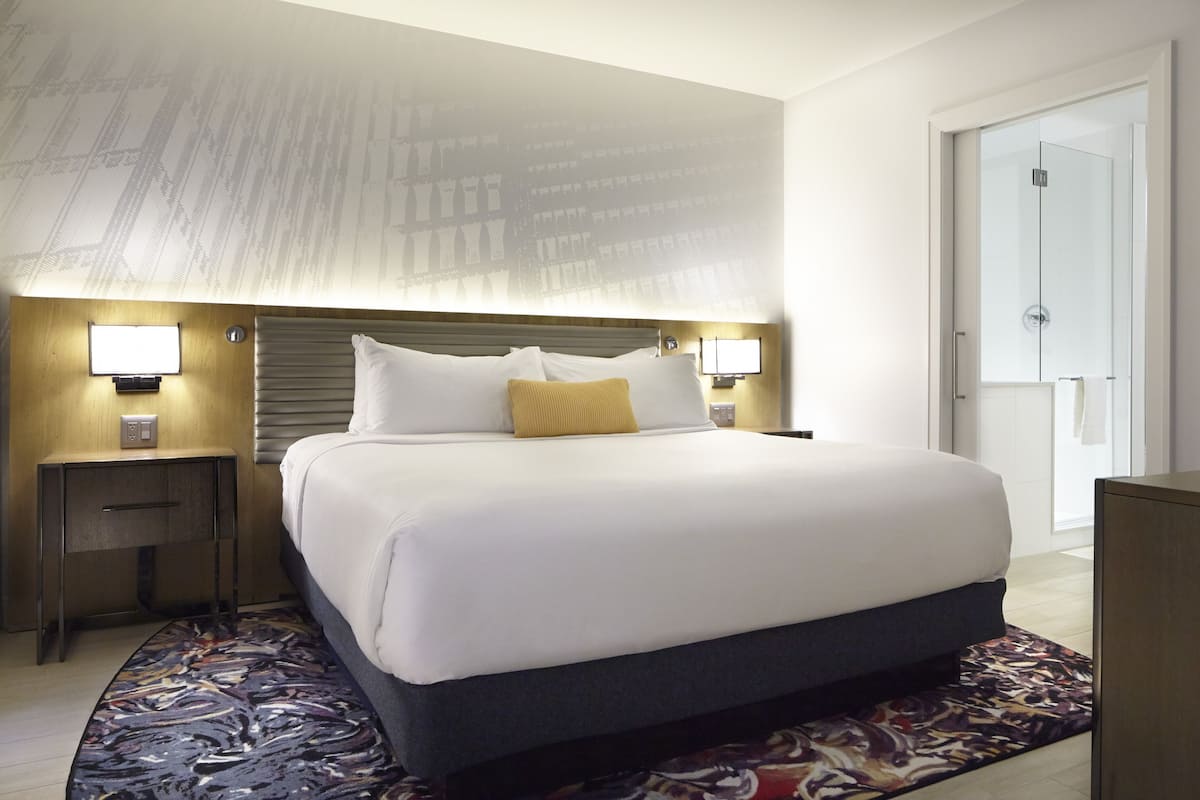 Habitación de hotel con una cama grande, dos mesitas de noche con lámparas, un tapete estampado y una puerta a la derecha.