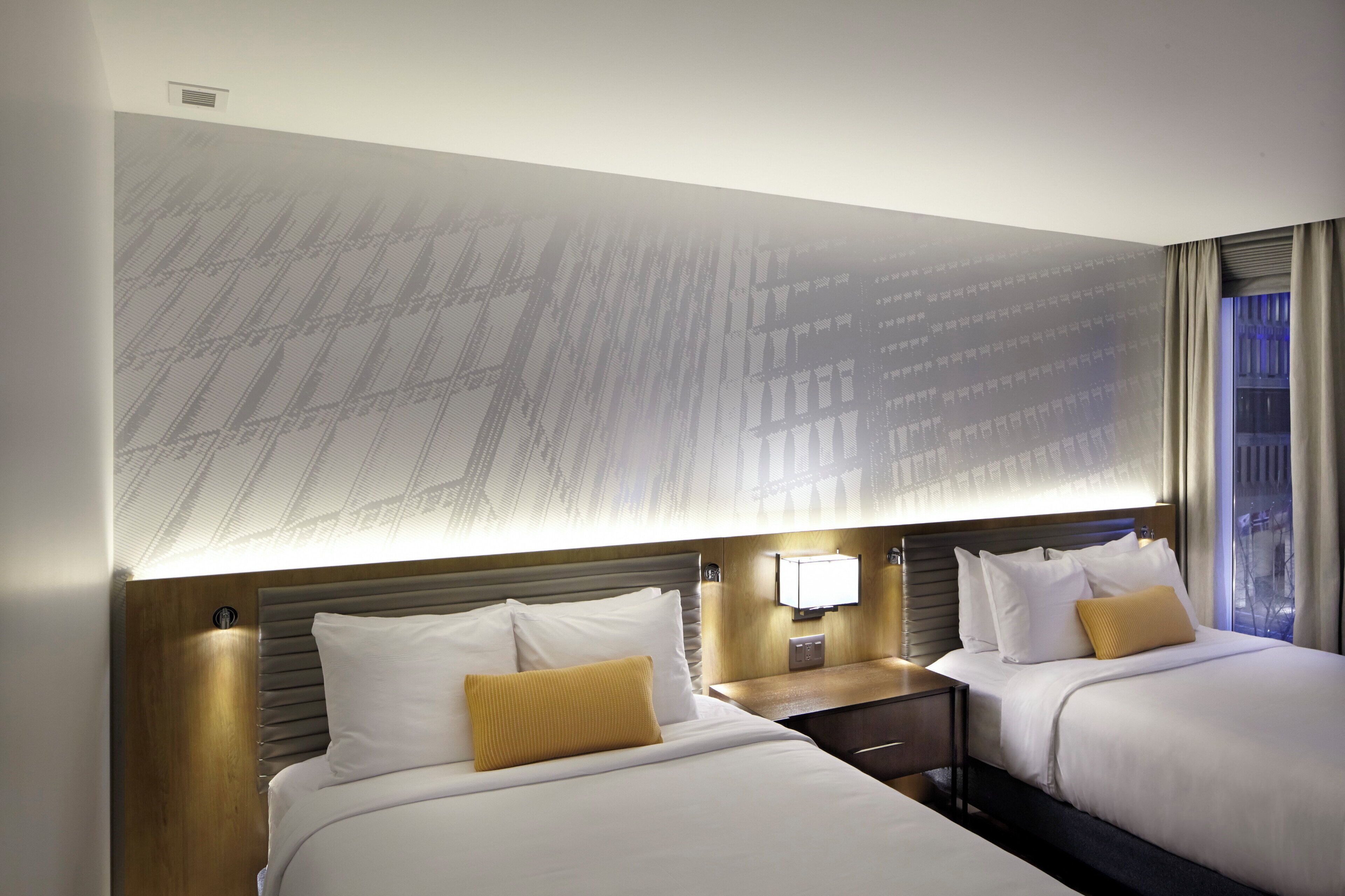 Habitación de hotel con dos camas, un ventanal grande y una lámpara fijada a la pared.