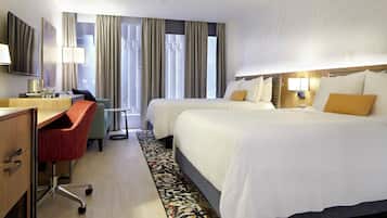 A hotel room with two beds, a desk, a chair, a TV, and a window with curtains.