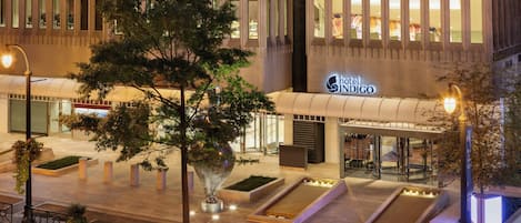 A hotel entrance with a modern facade, a large glass entrance, and a sign reading 'Hotel Indigo'.