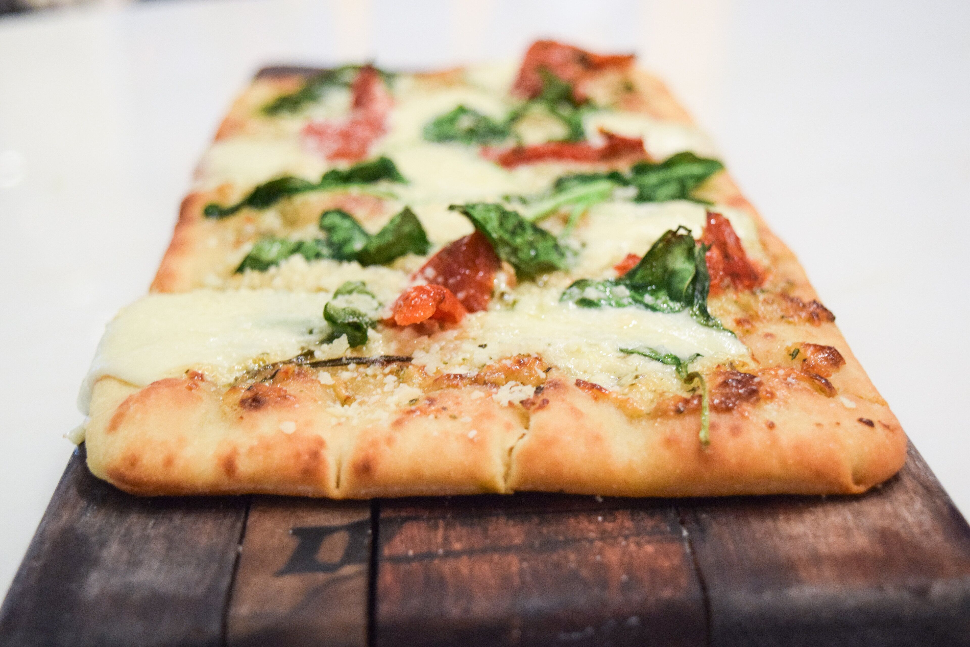 A rectangular pizza with toppings on a wooden surface.
