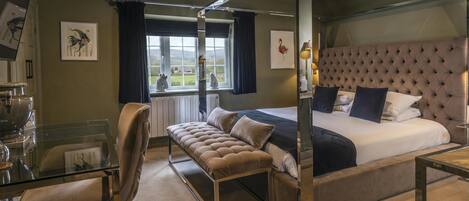 A bedroom with a four-poster bed, a sitting area with a bench, a desk with a chair, and a view of the outdoors through a window.
