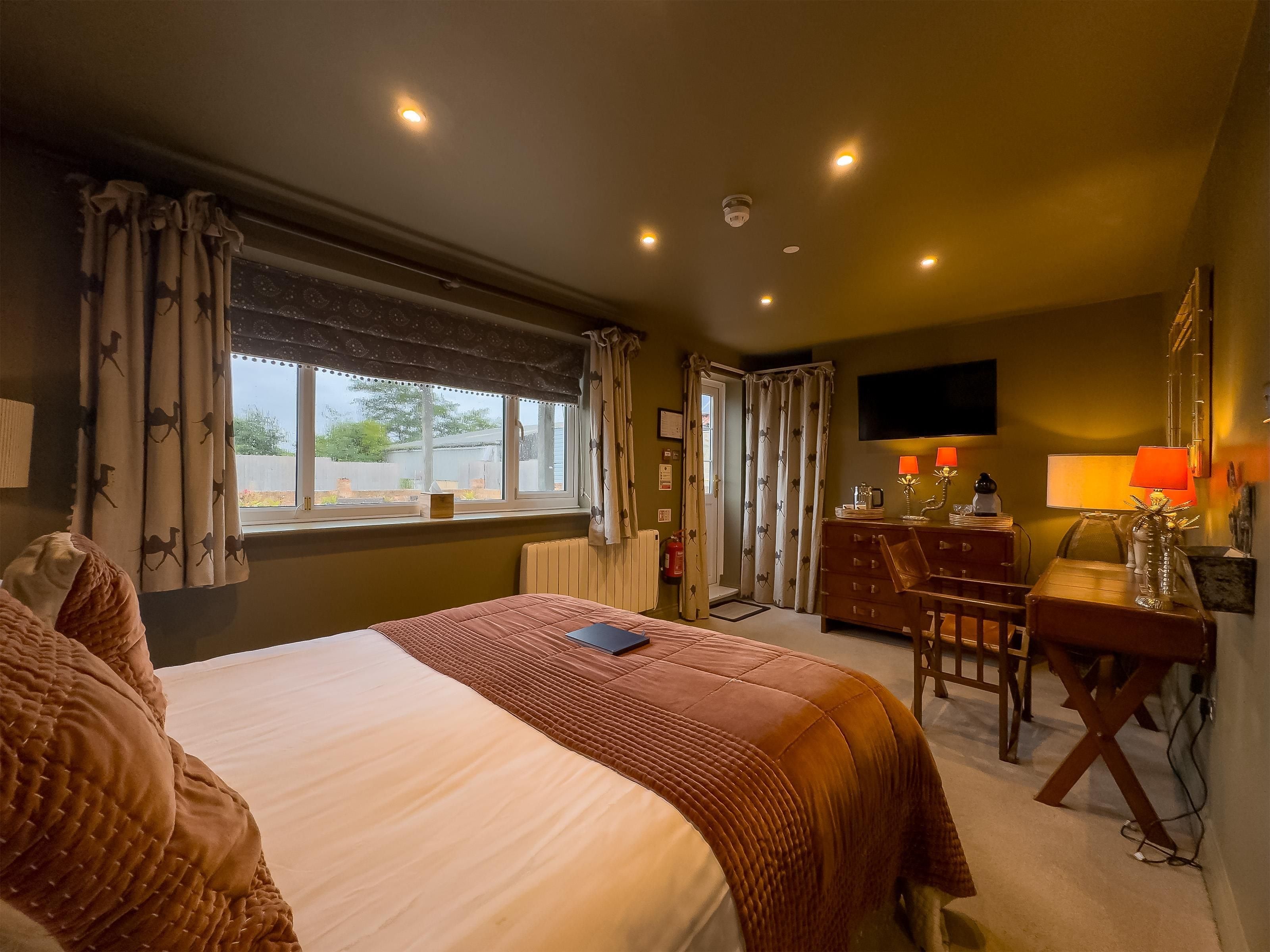 Una habitación de hotel con cama, escritorio, silla, televisión y ventana con cortinas.
