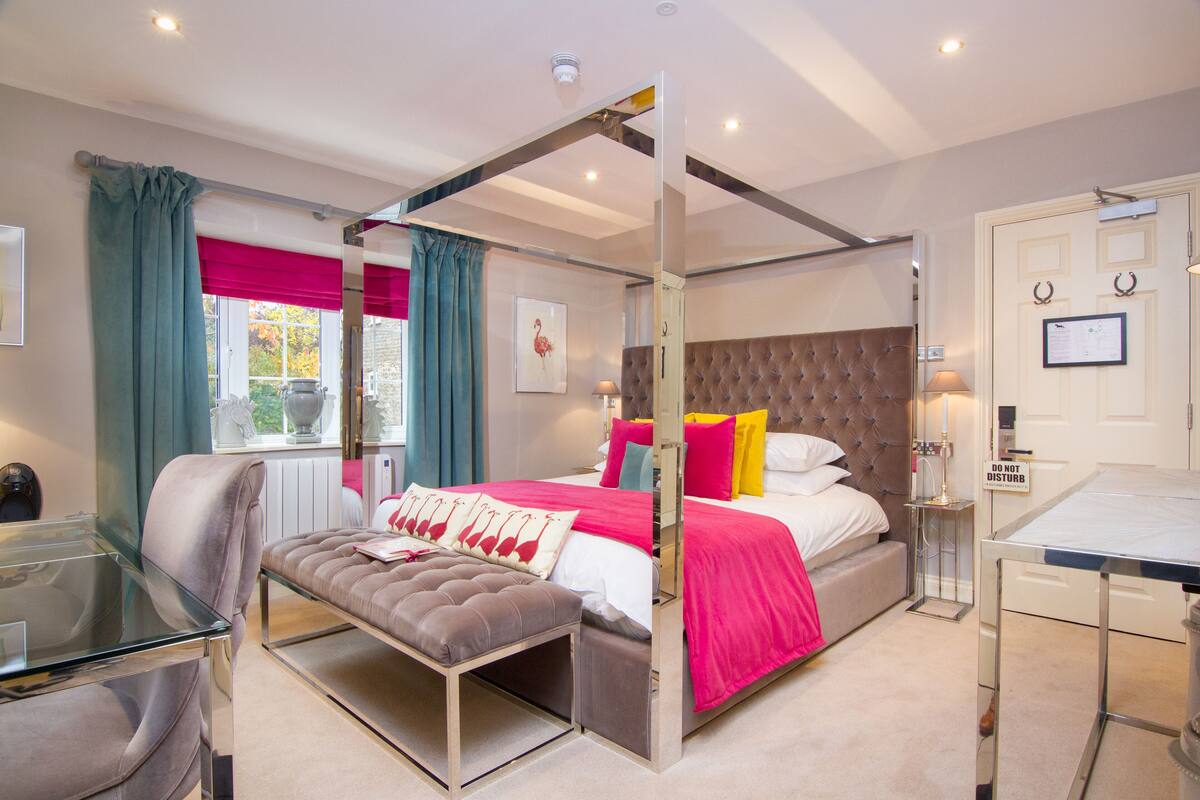 A modern bedroom with a four-poster bed, a glass desk, and a bench.