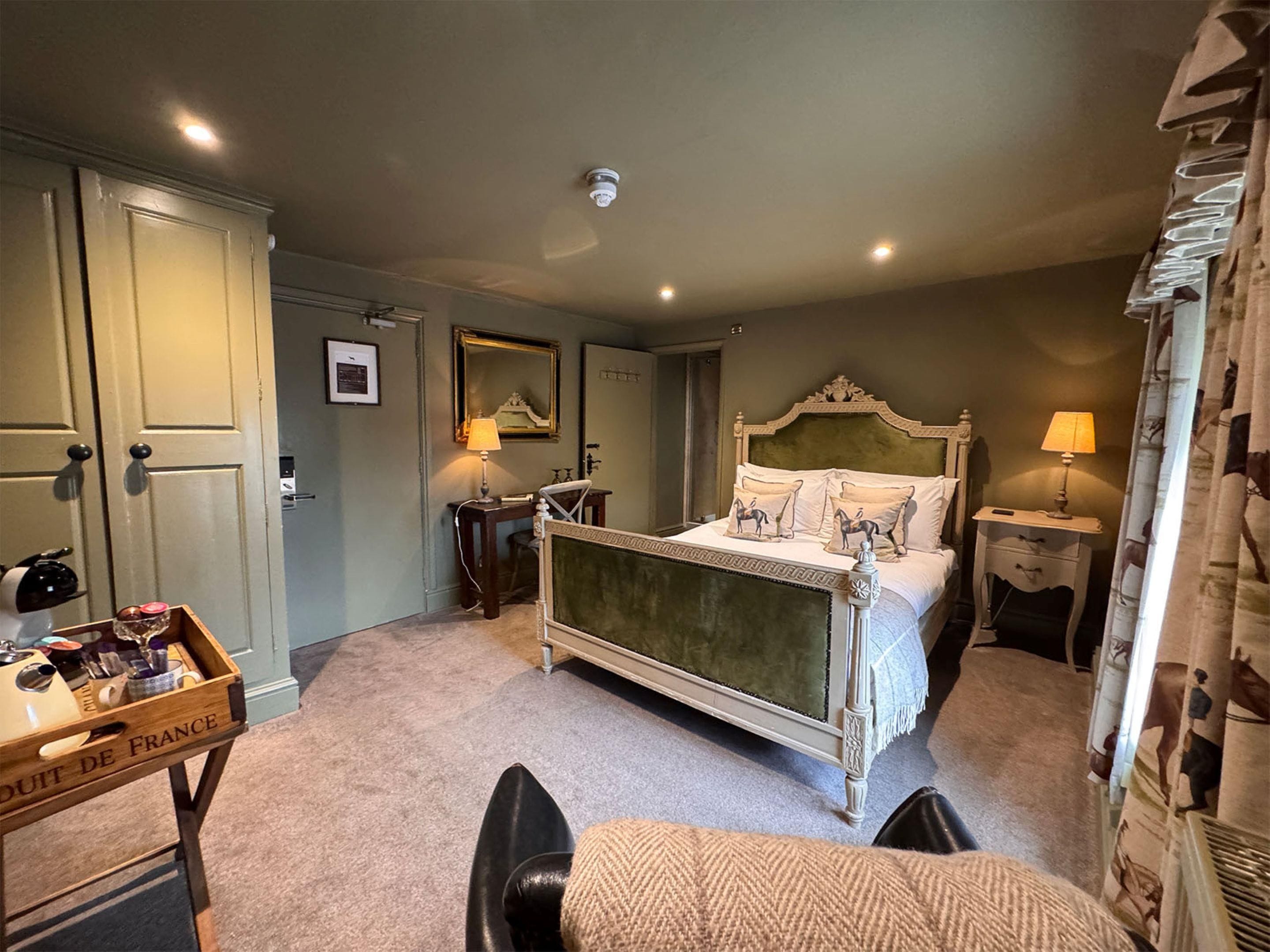 A hotel room with a bed, bedside tables, a desk with a lamp, a wardrobe, and a mirror.