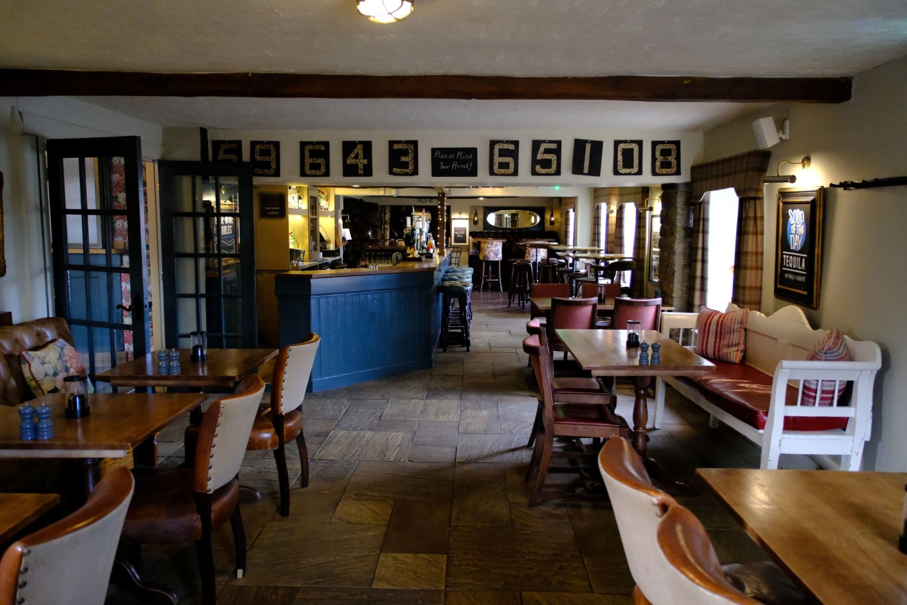 A restaurant interior with wooden tables and chairs, a bar area, and a seating section with a sofa.