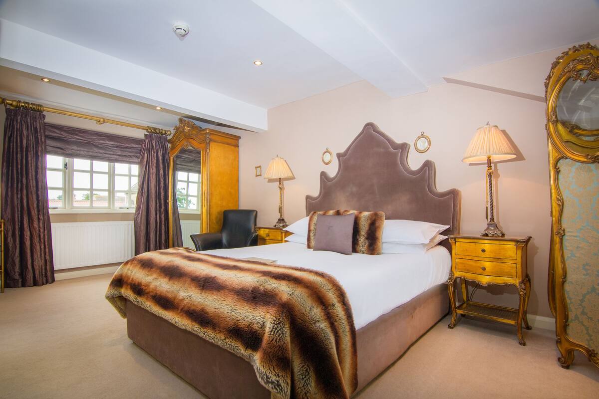 A spacious bedroom with a large bed, two bedside tables with lamps, a chair, and a large mirror.