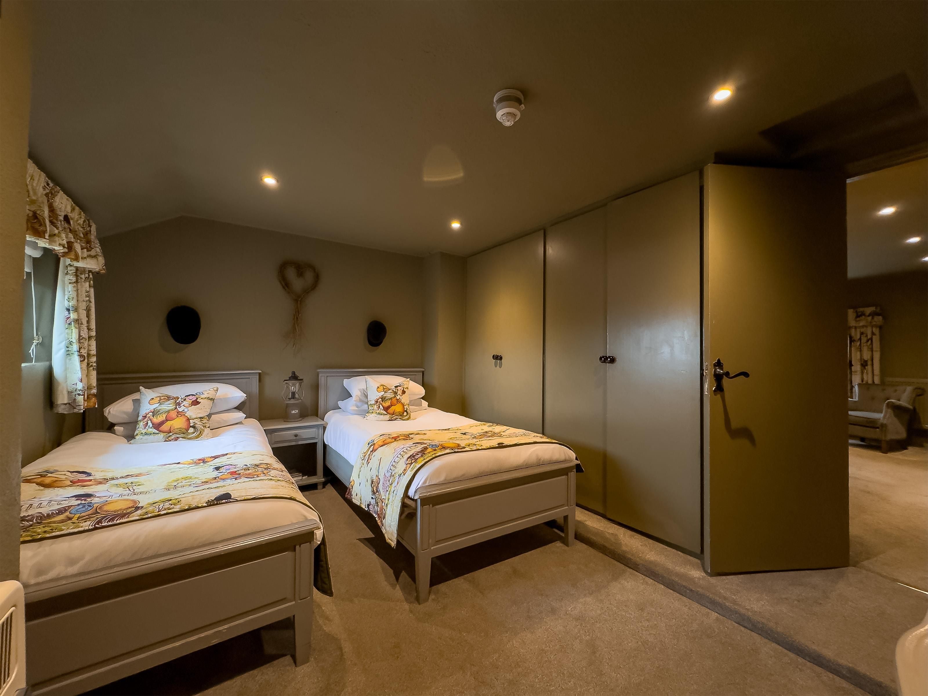 Une chambre avec deux lits, une armoire, une table de chevet avec une lampe et une décoration en forme de cœur accrochée au mur.