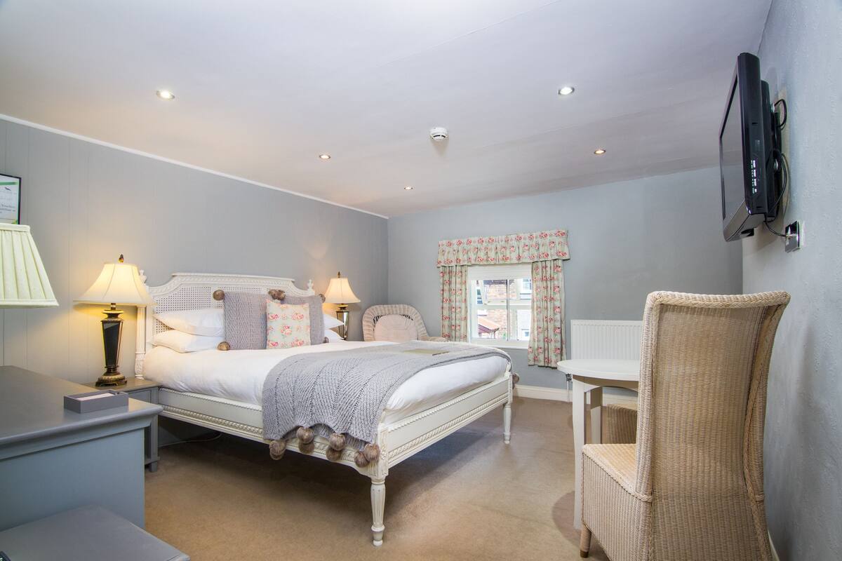 A bedroom with a bed, bedside tables, a chair, a desk, and a television mounted on the wall.