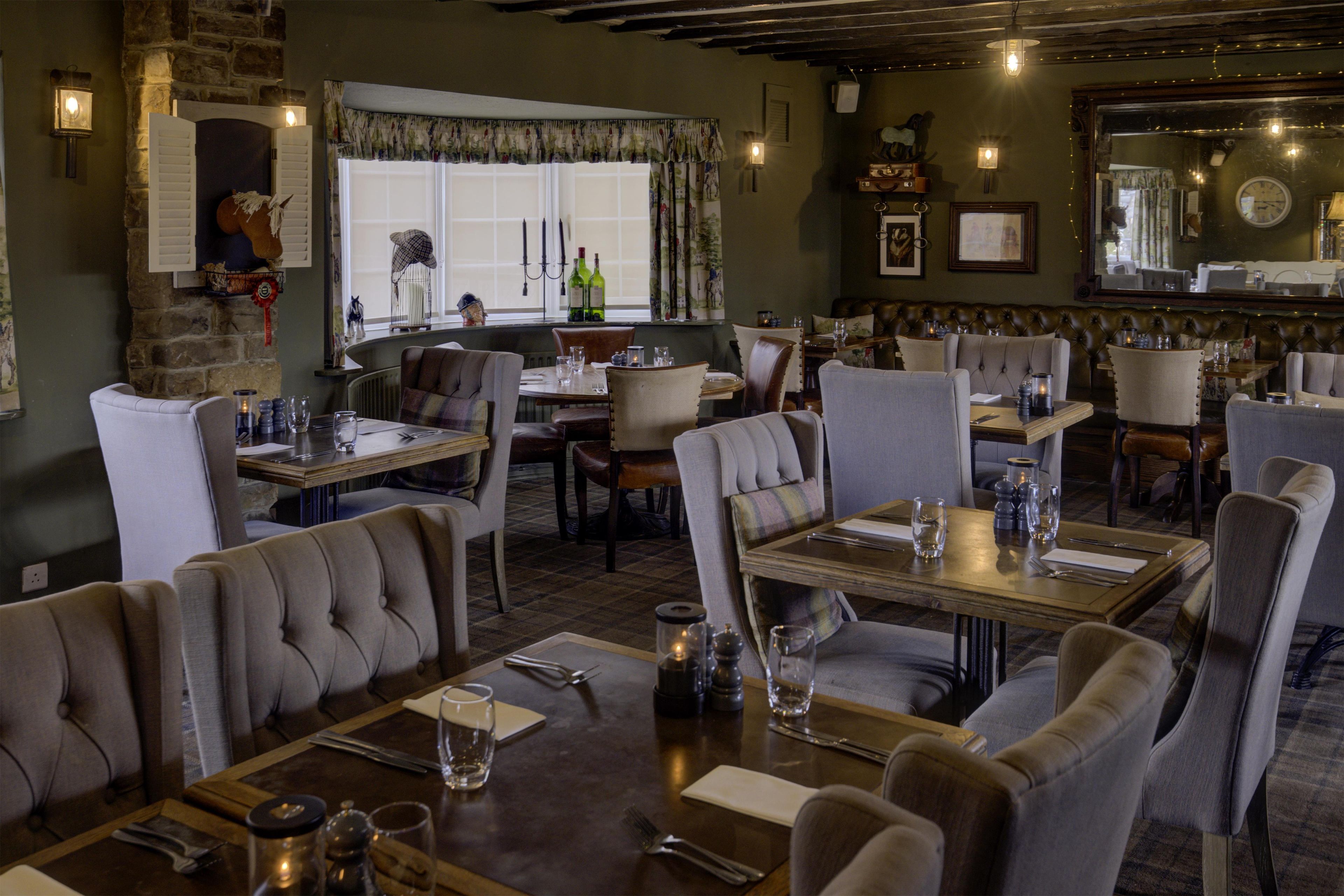 Een restaurant met meerdere eettafels en stoelen, een stenen muur en een groot raam met gordijnen.