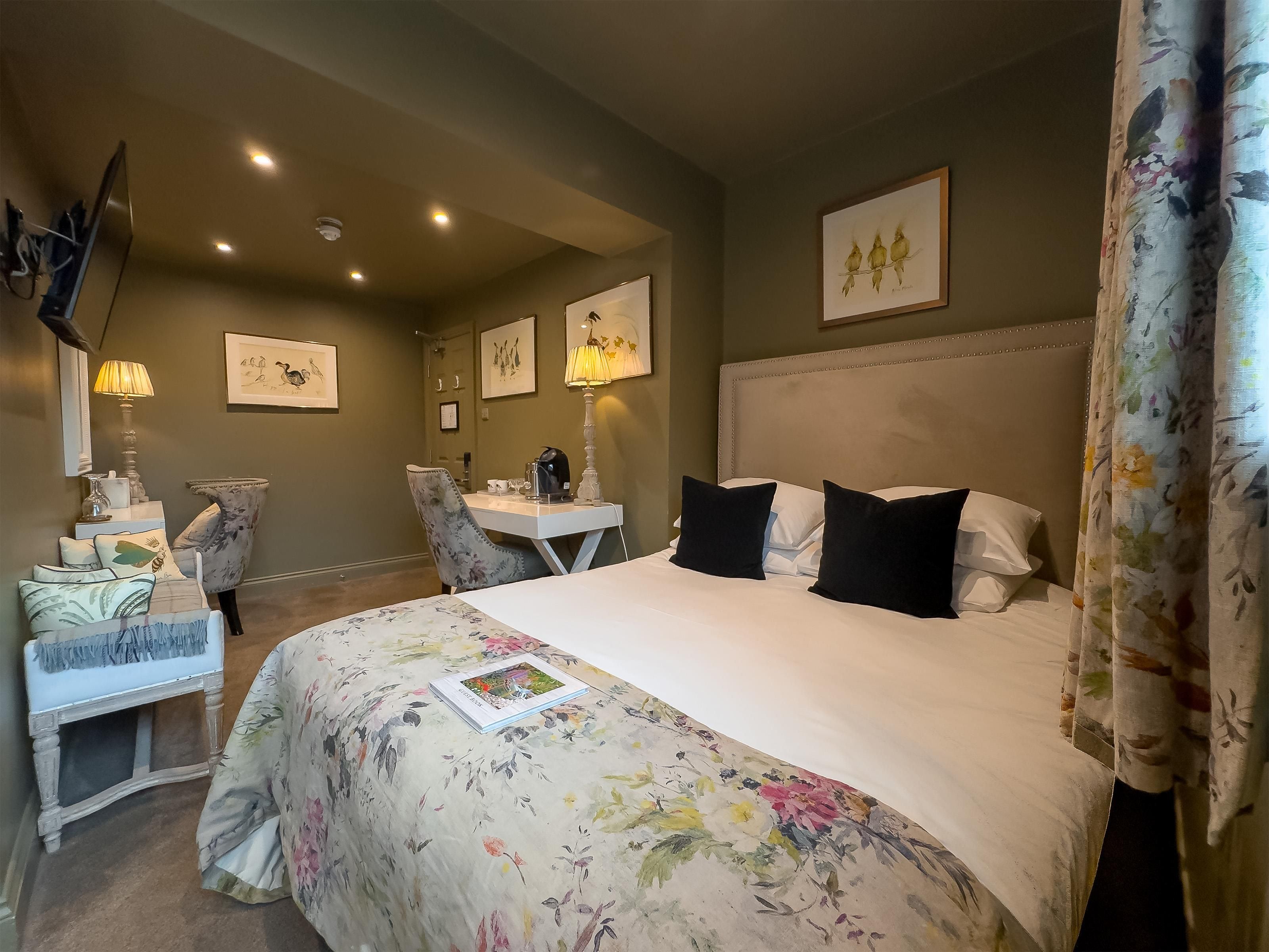 Habitación de hotel con una cama grande, un escritorio con silla, televisor y cuadros en las paredes.