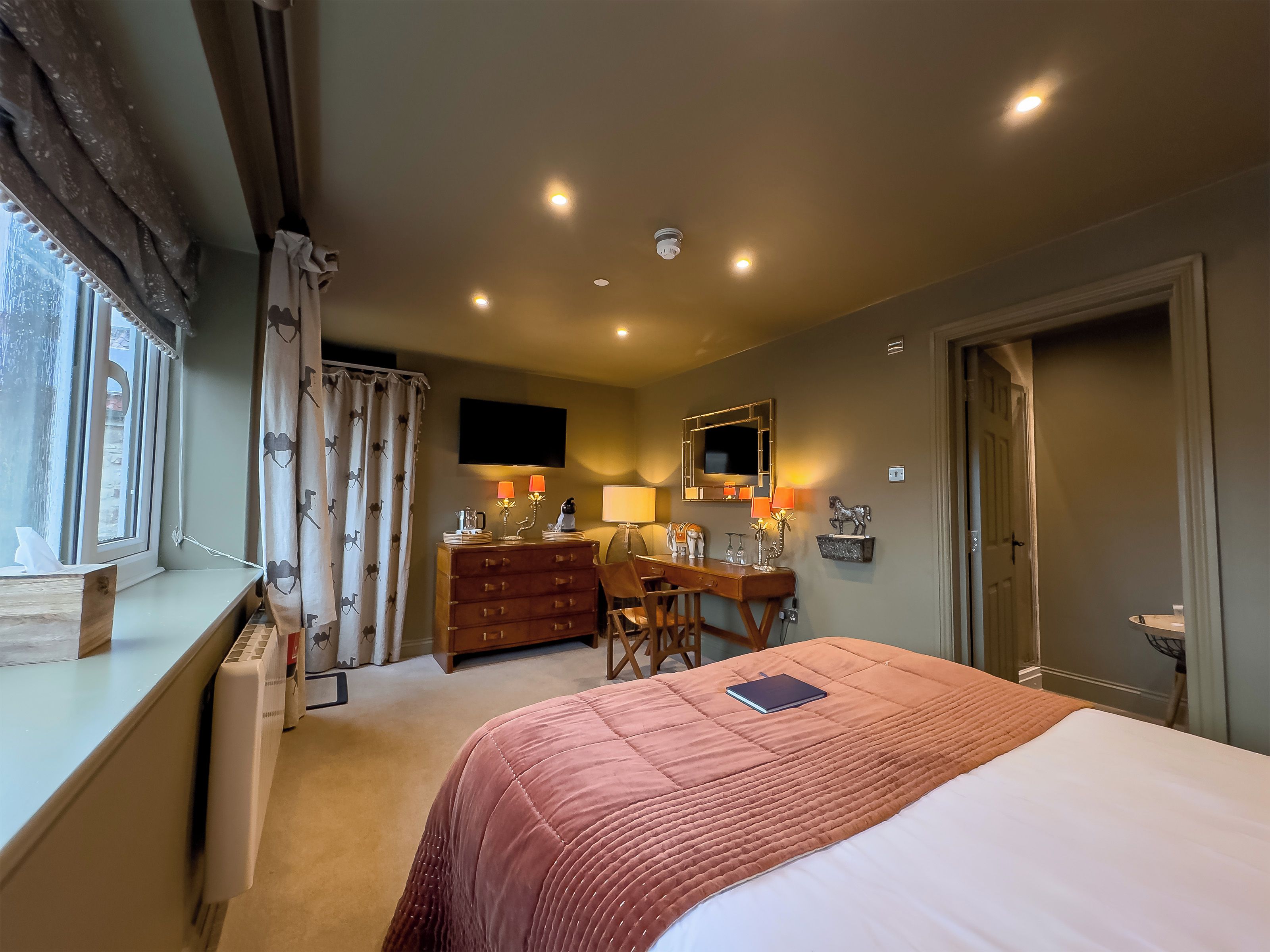 A bedroom with a bed, a desk, a dresser, a TV, and a door.