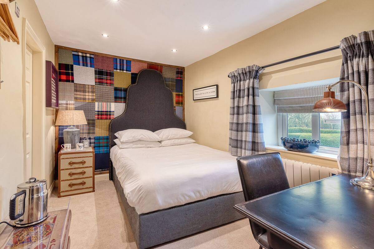 A bedroom with a bed, a desk, a lamp, a radiator, and a window with curtains.