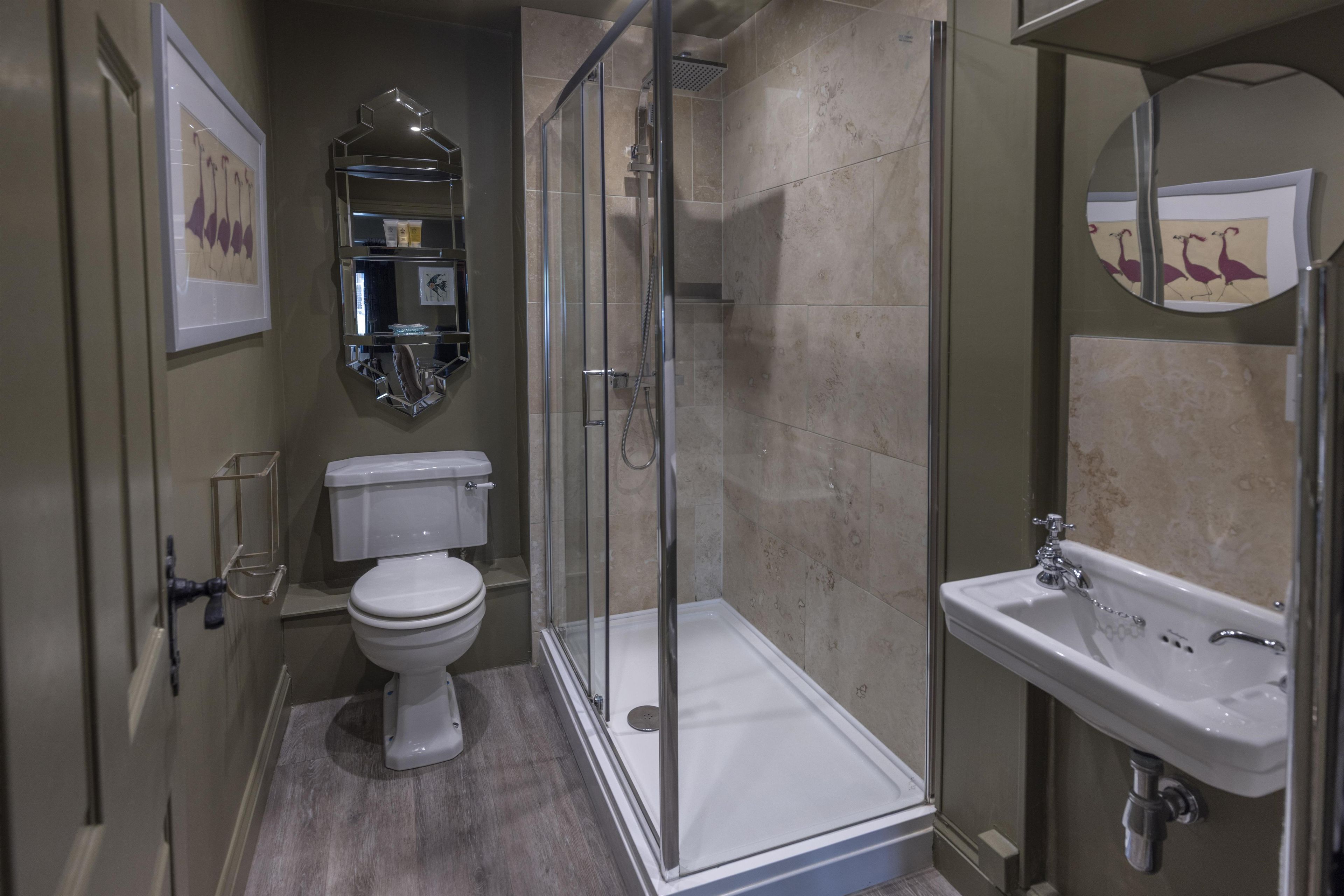 A modern bathroom with a glass-enclosed shower, a white toilet, a sink with a mirror, and a shelf with toiletries.