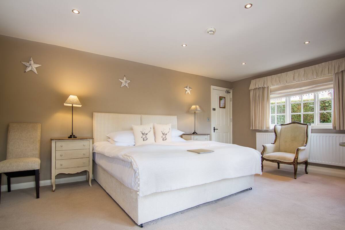 A bedroom with a large bed, two bedside tables, a chair, and a window with curtains.