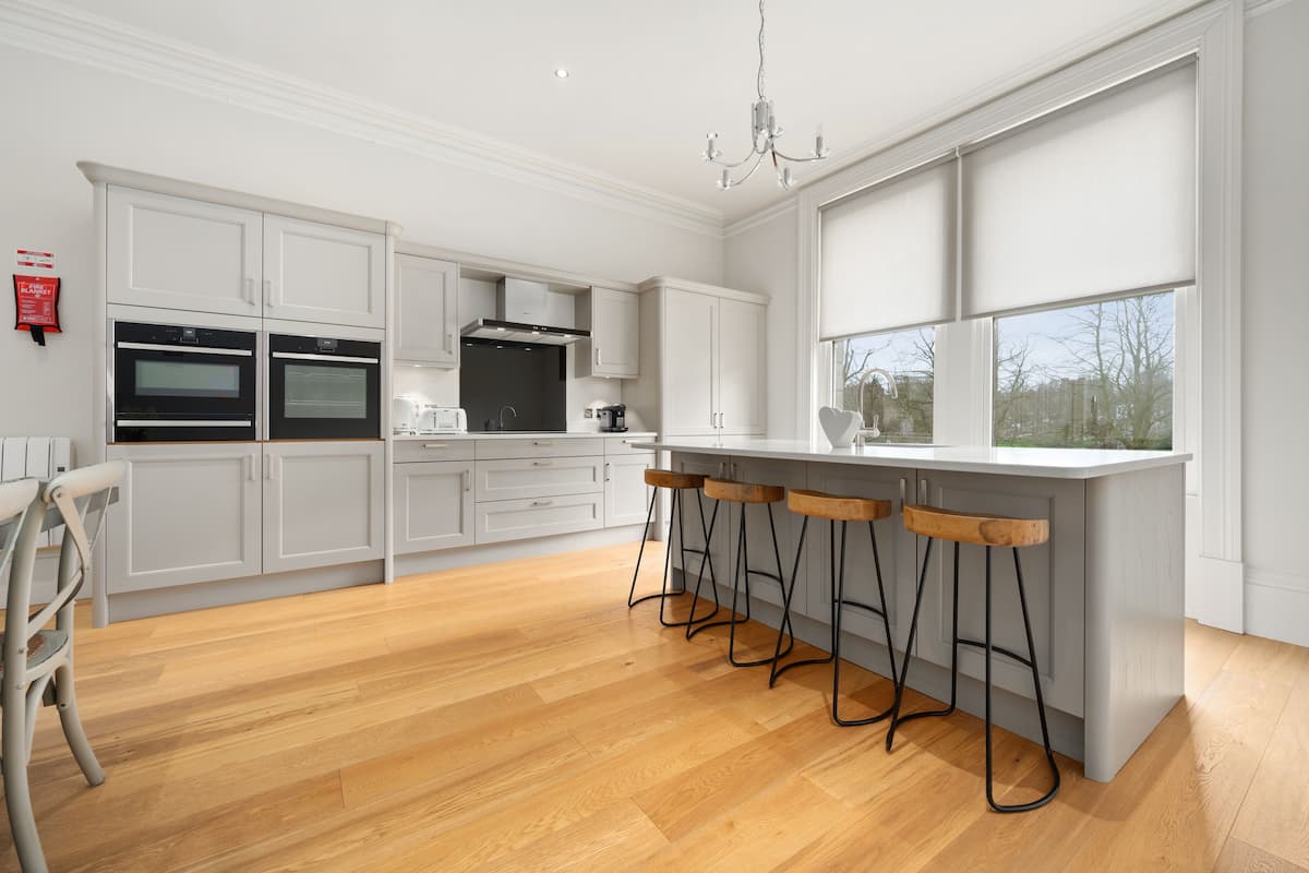 A modern kitchen with white cabinetry, a central island with bar stools, and a large window providing natural light.