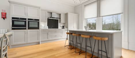 A modern kitchen with white cabinetry, a central island with bar stools, and a large window providing natural light.