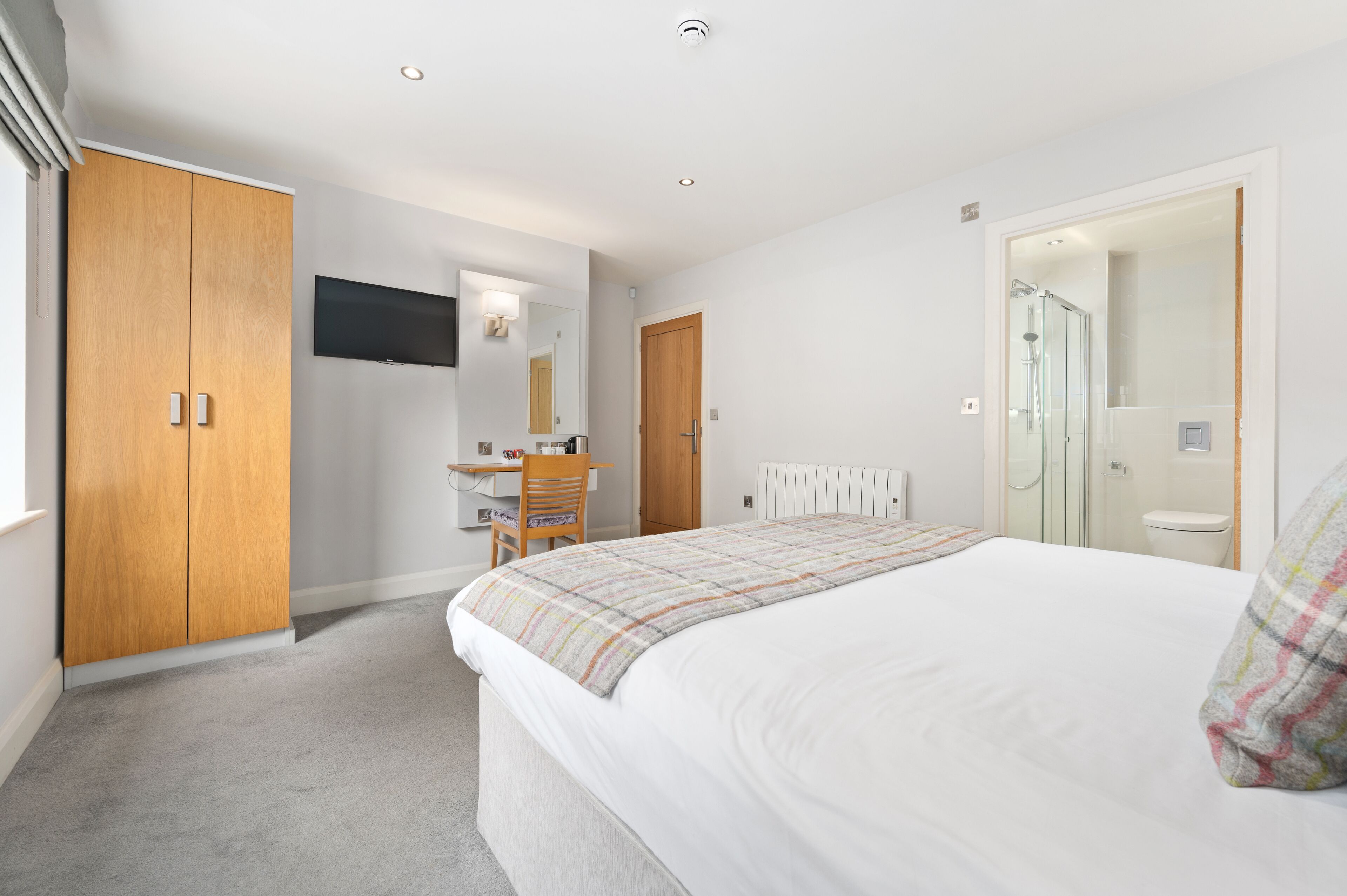 A bedroom with a bed, a desk, a chair, a TV, and a wardrobe.