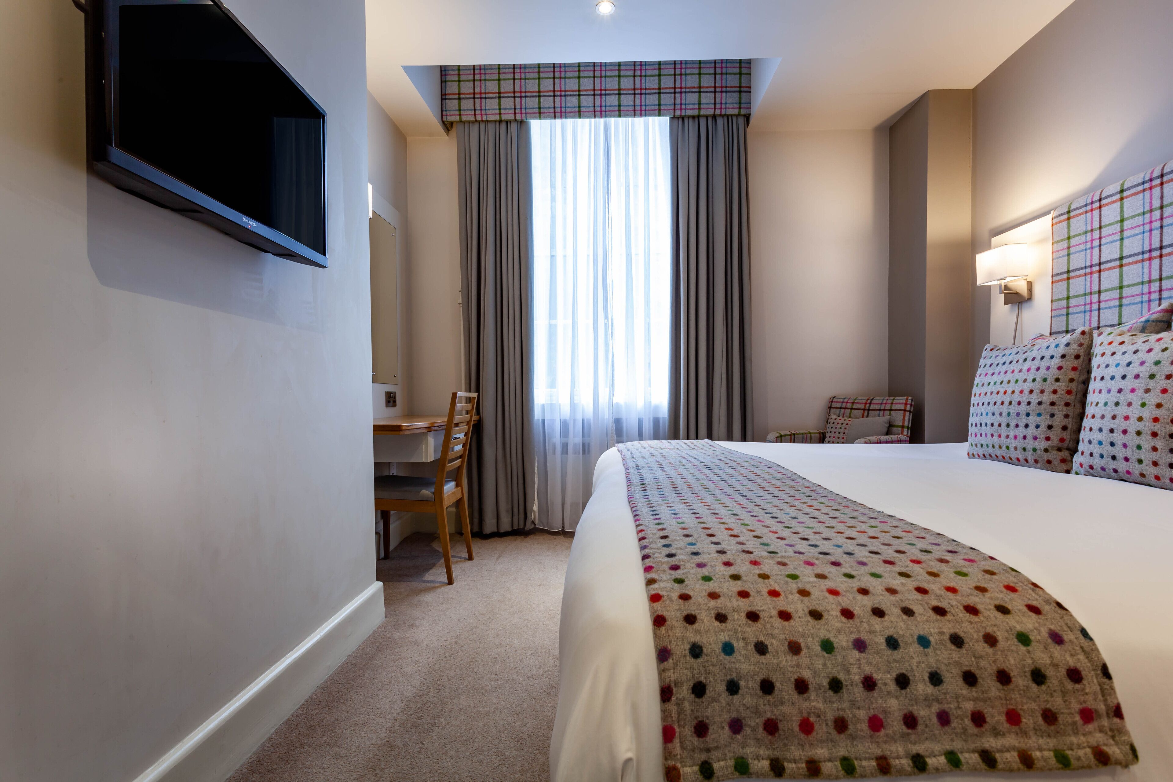 A hotel room with a large bed, a desk, and a chair.