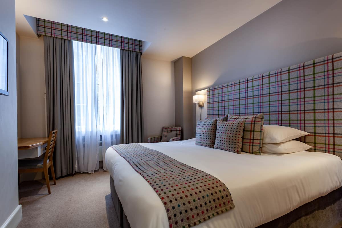 A hotel room with a large bed, a desk, and a chair.