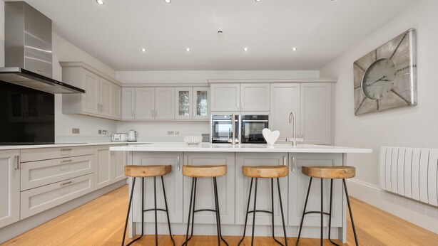 A modern kitchen with white cabinets, a central island with stools, stainless steel appliances, and a wall clock.