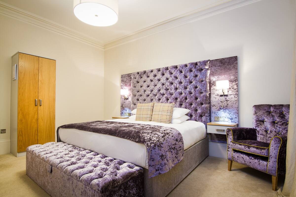 Quarto com uma cama grande, um guarda-roupa de madeira, uma cabeceira estofada e uma mesa de cabeceira com abajur.