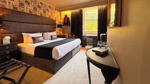 A hotel room with a large bed, a desk, a chair, a dresser, and a window with curtains.