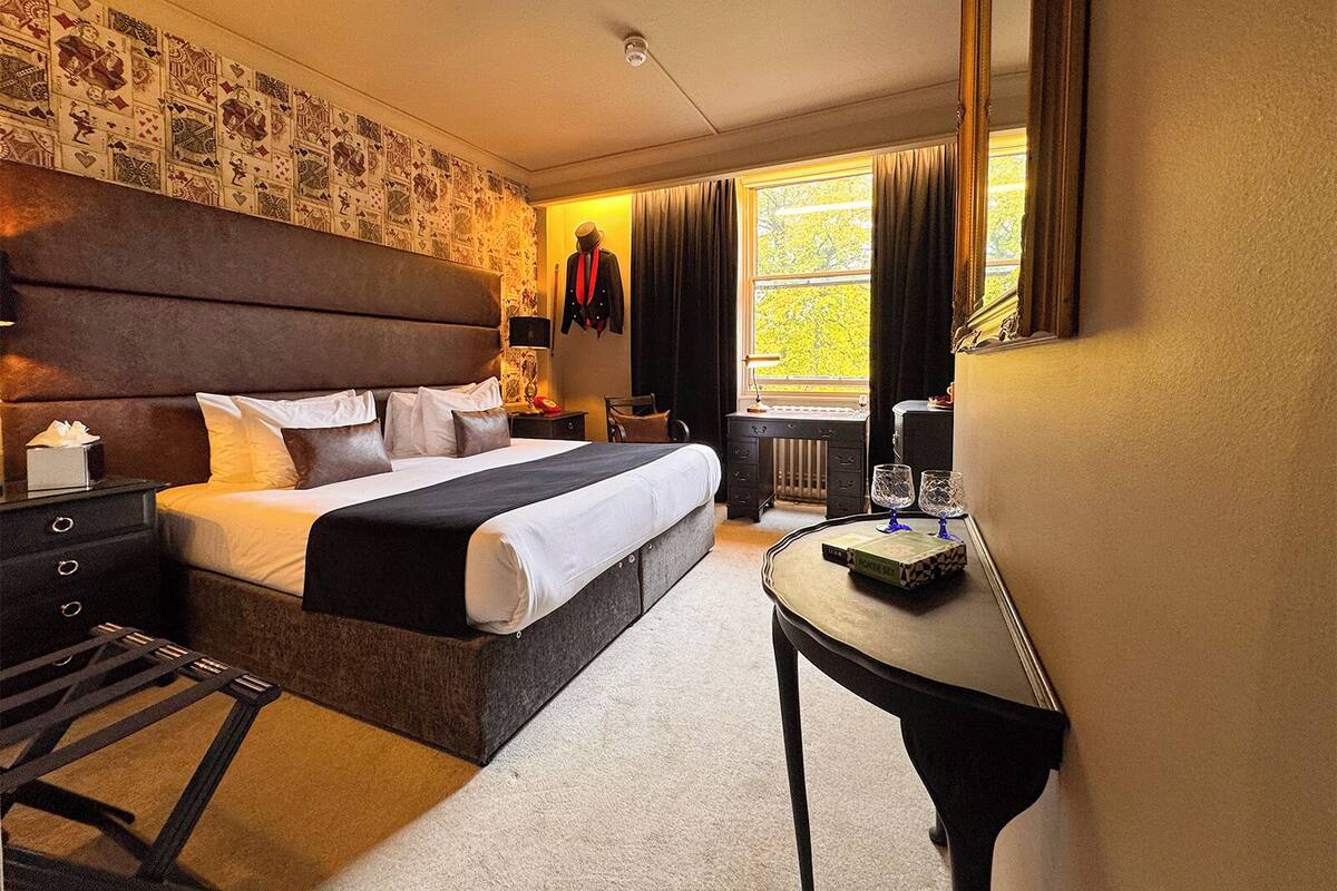 A hotel room with a large bed, a desk, a chair, a dresser, and a window with curtains.