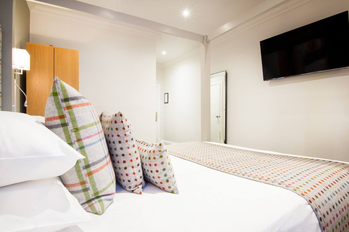Quarto de hotel com cama, almofadas, televisão e guarda-roupa.