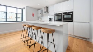 A modern kitchen with white cabinetry, a central island with stools, and a large window providing natural light.