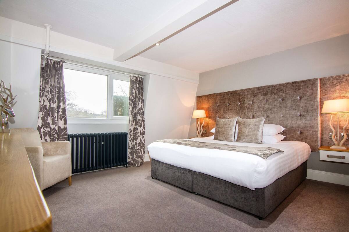 A modern bedroom with a large bed, a chair, a radiator, and a window with curtains.