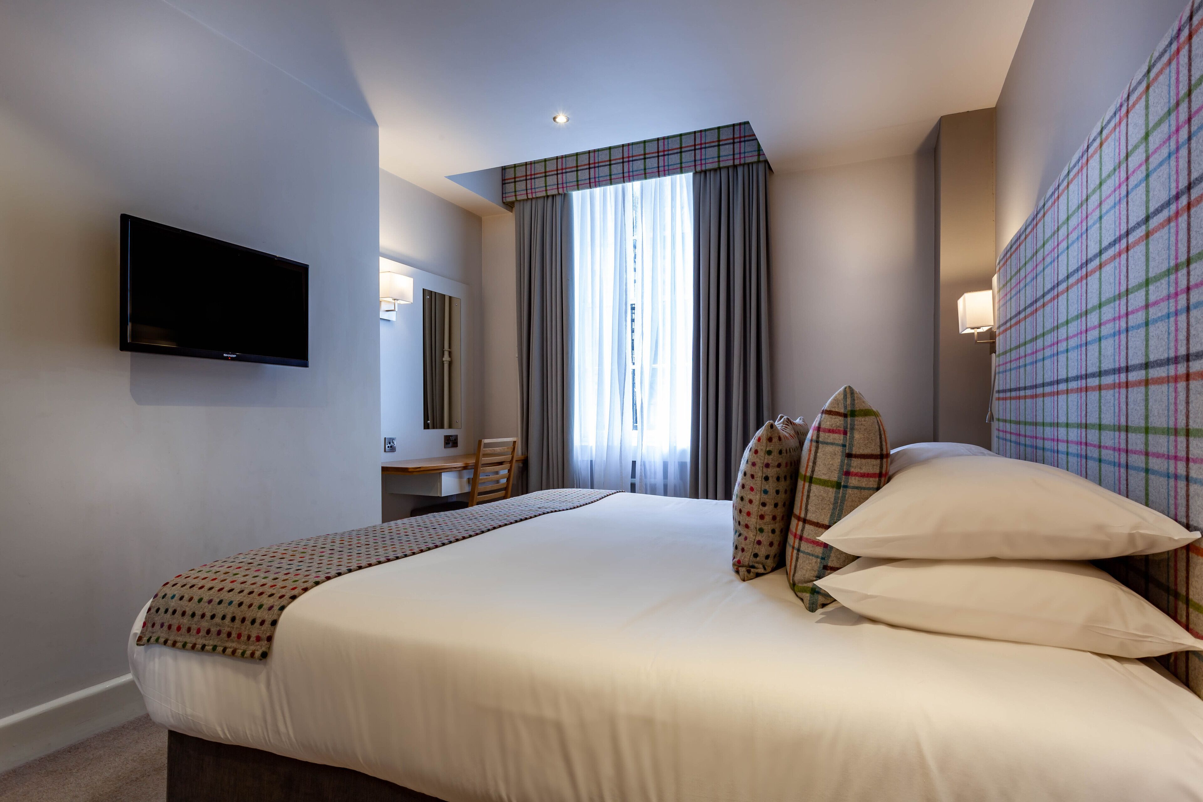 A hotel room with a bed, a desk, a chair, a television, and a window with curtains.