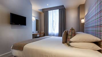 A hotel room with a bed, a desk, a chair, a television, and a window with curtains.