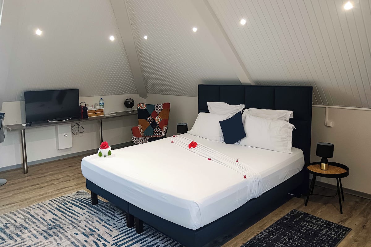 A modern bedroom with a large bed, a flat-screen TV, a desk, and a chair.