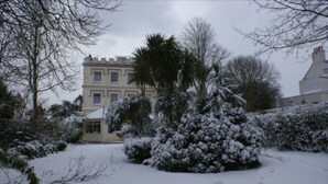 A snow-covered garden with a building in the background. - Grange Lodge Hotel (St. Peter Port)