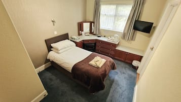 Una habitación de hotel con cama, escritorio con silla, televisor y ventana con cortinas.