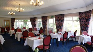 A formal dining room with multiple tables and chairs, a chandelier, and a fire exit sign. - Grange Lodge Hotel (St. Peter Port)