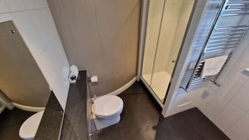 Un baño pequeño con inodoro, cabina de ducha de vidrio y toallero.