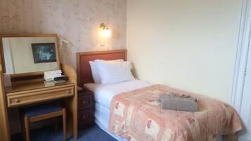 Una habitación de hotel con un escritorio de madera, una cama con colcha estampada, una mesita de noche y una lámpara de pared.