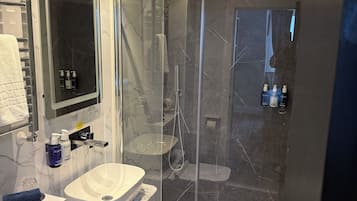 Un baño moderno con ducha de vidrio, lavamanos blanco y salpicadero de mármol.