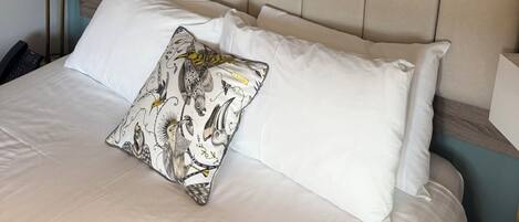 Een keurig opgemaakt bed met witte lakens en een decoratief kussen, een houten hoofdbord, een bedlampje en een lijst met een foto van een brug aan de muur.