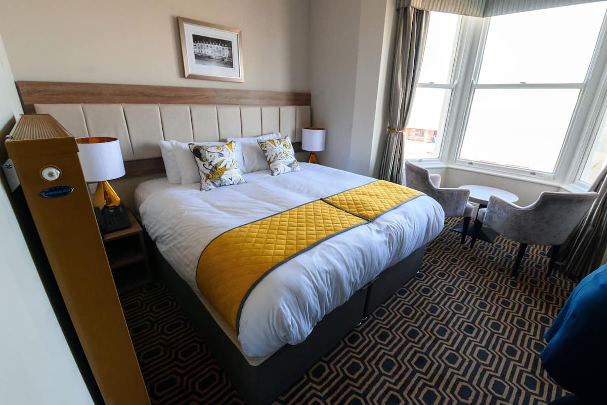 Habitación de hotel con una cama grande, dos mesitas de noche con lámparas, una mesita redonda y una silla.