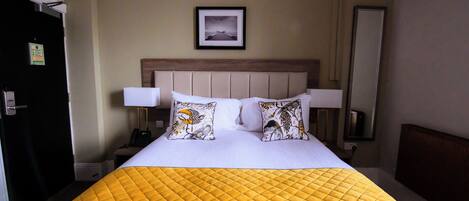 A hotel room with a bed, a nightstand, a lamp, a framed picture on the wall, and a door.