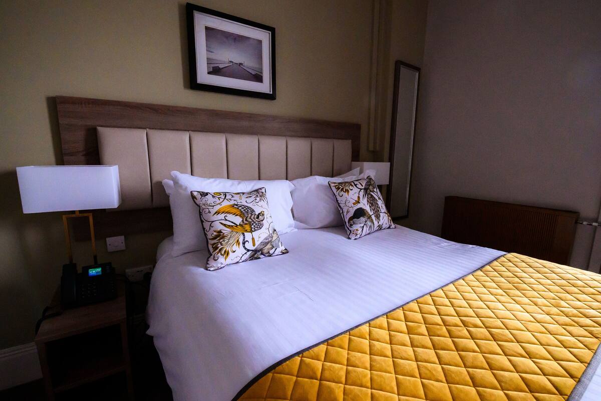 Una habitación de hotel con una cama, una mesita de noche con lámpara y un cuadro enmarcado en la pared.