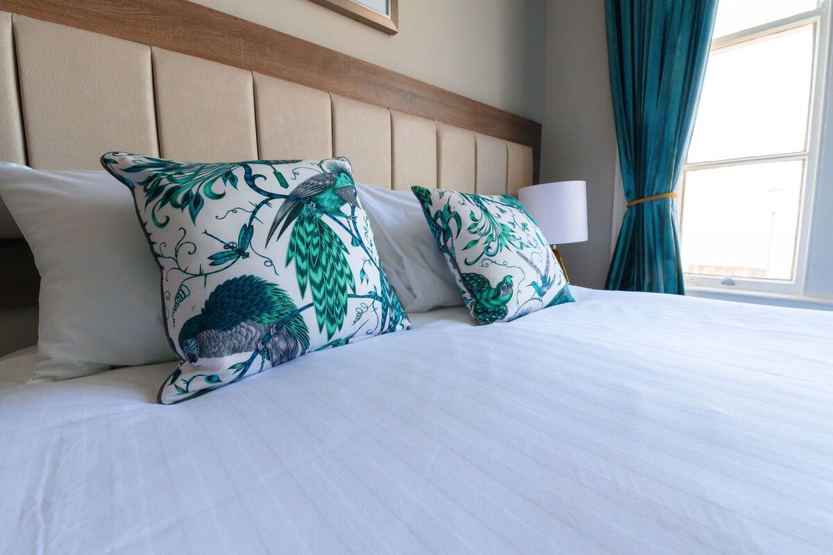 Una cama con ropa de cama blanca y almohadas decorativas con estampado de pájaros.