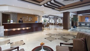 A hotel lobby with a reception desk, seating area, and a large potted plant. - Swiss Inn Plaza (6th of October City)