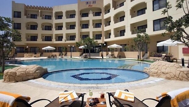 A hotel with a swimming pool, lounge chairs, and umbrellas. - Swiss Inn Plaza (6th of October City)