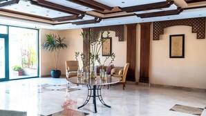 A spacious lobby with a round table, chairs, potted plants, and a large window. - Swiss Inn Plaza (6th of October City)